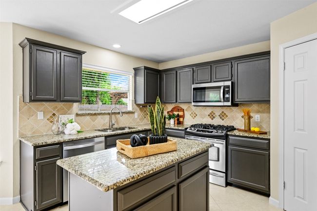 Kitchen with stainless steel appliances, light stone countertops, a center island, and decorative backsplash | Image 16