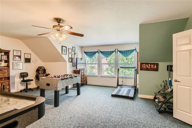 Playroom with baseboards, vaulted ceiling, carpet flooring, a textured ceiling, and a ceiling fan | Image 26