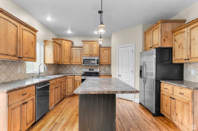 Kitchen featuring appliances with stainless steel finishes, light wood-style floors, a kitchen island, and a sink | Image 4