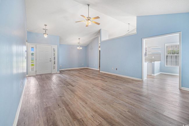Unfurnished living room featuring a ceiling fan, wood finished floors, a chandelier, and high vaulted ceiling | Image 11