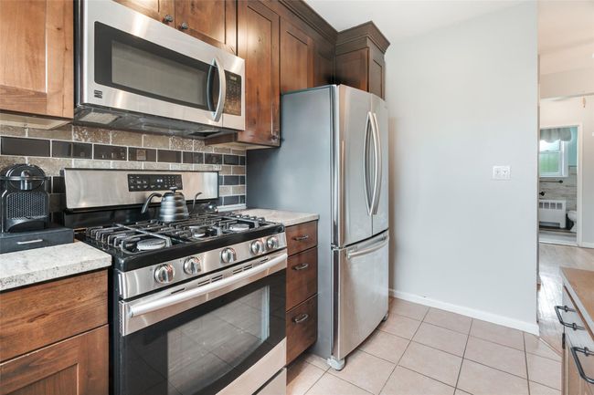 Kitchen with stainless steel appliances, radiator heating unit, decorative backsplash, baseboards, and light tile patterned floors | Image 6