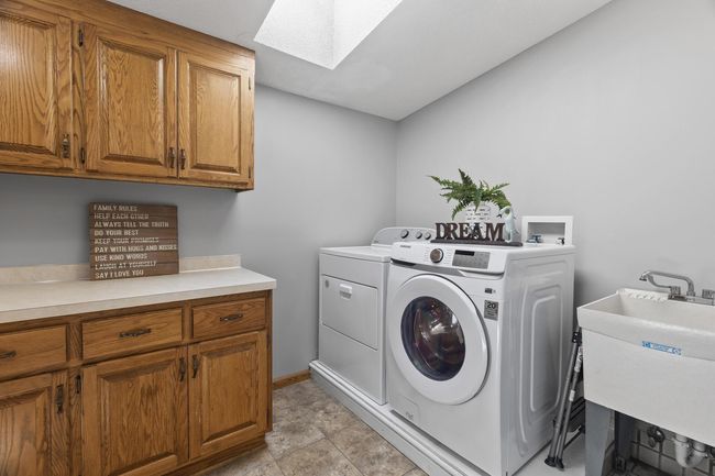 Convenient upper-level laundry room featuring a folding table, built-in cabinets, sink, built-in ironing board, and new/newer electric washer and dryer—perfectly located near the main bedrooms. | Image 29
