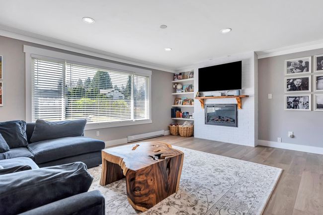 Living room with a baseboard heating unit, a fireplace, baseboards, ornamental molding, and wood finished floors | Image 10