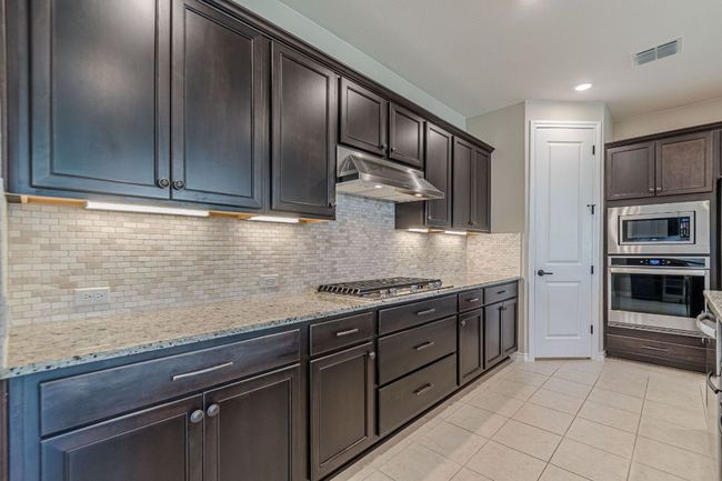 Kitchen featuring backsplash, light tile patterned flooring, stainless steel appliances, light stone countertops, and under cabinet range hood | Image 15