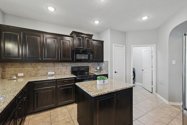 Kitchen featuring decorative backsplash, black appliances, arched walkways, and light tile patterned flooring | Image 8