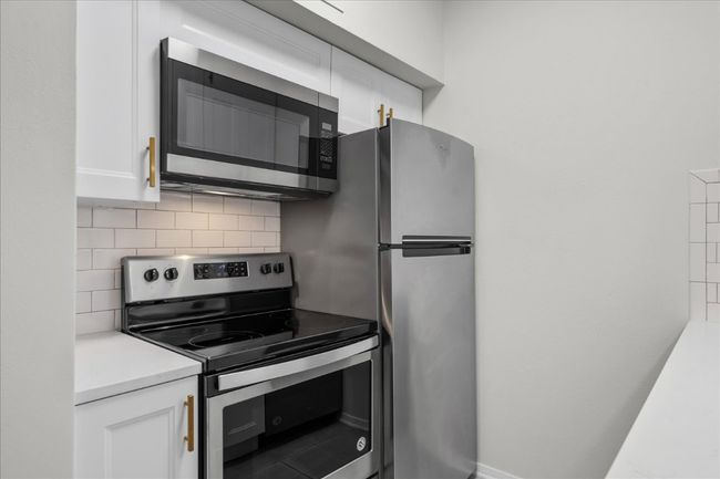 Kitchen with stainless steel appliances, tasteful backsplash, white cabinetry, and light countertops | Image 15