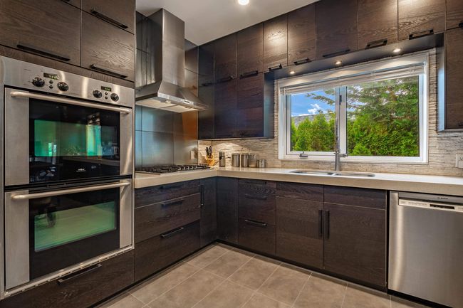 Kitchen with appliances with stainless steel finishes, wall chimney range hood, light countertops, and backsplash | Image 12