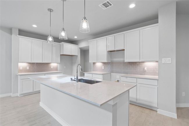 This stunning kitchen displays such beautiful stained cabinets, custom neutral paint, quartz countertops, modern backsplash, oversized kitchen island with extra storage, breakfast bar, recessed and pendant lighting, high ceilings and walk in pantry. | Image 6