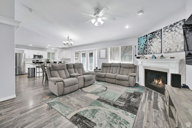 Living room with ceiling fan with notable chandelier, vaulted ceiling, wood finished floors, and a glass covered fireplace | Image 8