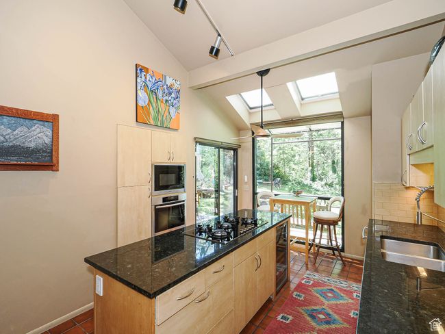 Kitchen featuring black appliances, vaulted ceiling, light brown cabinets, a skylight, and a center island | Image 22