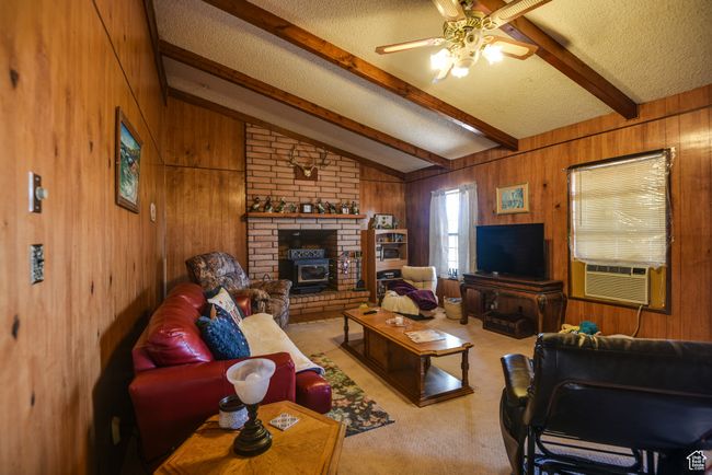 Living area featuring wood walls, a textured ceiling, a ceiling fan, cooling unit, and a wood stove | Image 23