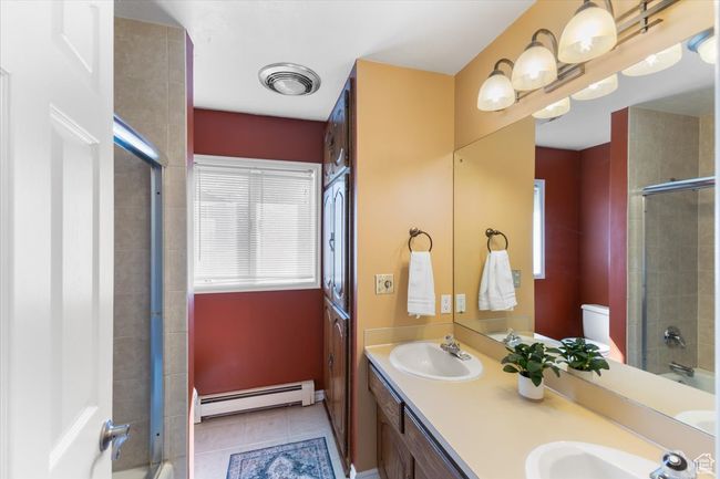 Bathroom featuring an enclosed shower, a baseboard heating unit, a sink, and visible vents | Image 12