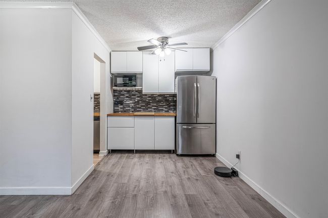 Kitchen with freestanding refrigerator, a ceiling fan, crown molding, black microwave, and white cabinetry | Image 6