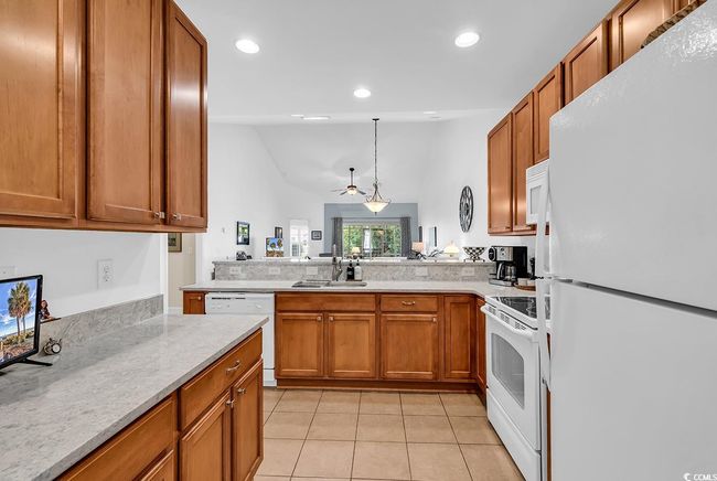 Kitchen featuring white appliances, light tile patterned floors, light countertops, a peninsula, and brown cabinets | Image 6