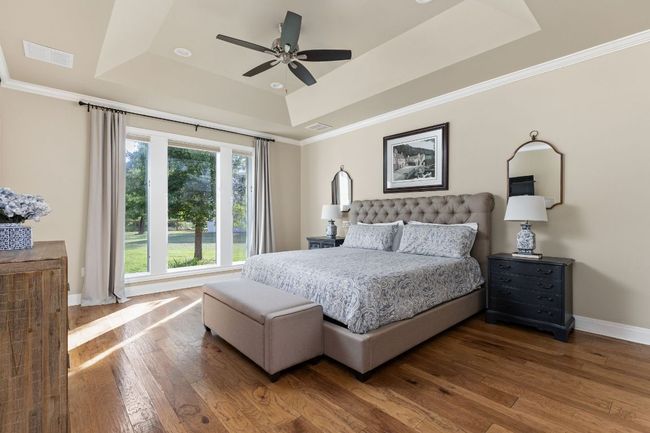 The serene primary suite offers a peaceful retreat with large windows that overlook the lush property. | Image 15