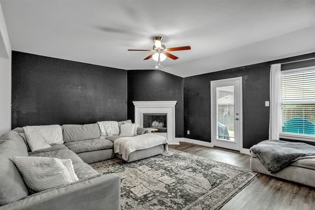 Living area with wood finished floors, lofted ceiling, ceiling fan, a textured wall, and a fireplace with raised hearth | Image 11