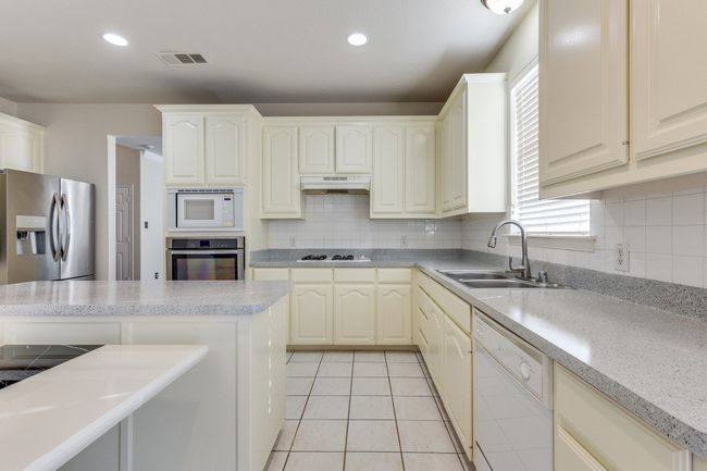 Kitchen with a sink, under cabinet range hood, stainless steel appliances, light tile patterned floors, and visible vents | Image 14