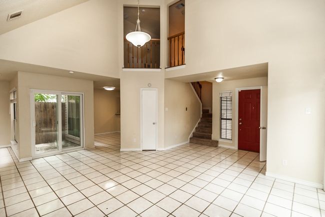 Unfurnished living room with high vaulted ceiling, light tile patterned floors, and stairway | Image 4