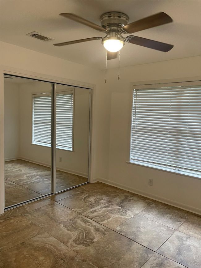 Unfurnished bedroom with mirrored closet, ceiling fan, and stone finish floors | Image 12