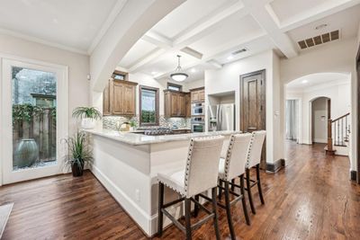 Kitchen featuring a Kithcen Island, Abundant Cabinet Space and Counter Space, stainless steel appliances, gas cooktop, Beverage Cooler, & a Coffered Ceiling | Image 1