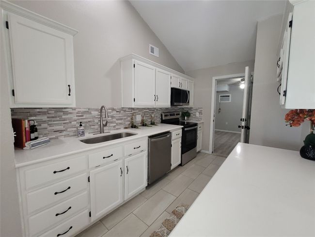 Kitchen with appliances with stainless steel finishes, a sink, tasteful backsplash, lofted ceiling, and white cabinetry | Image 10