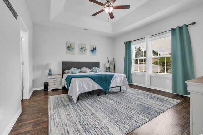 Bedroom featuring dark wood-style floors, ceiling fan, a raised ceiling, baseboards, and visible vents | Image 29