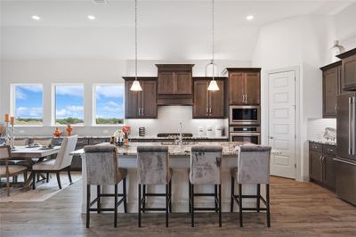 Kitchen featuring dark hardwood / wood-style floors, tasteful backsplash, an island with sink, stainless steel appliances, and light stone counters | Image 2