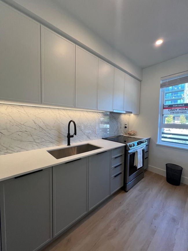 Kitchen featuring a sink, gray cabinetry, light wood finished floors, range with electric stovetop, and backsplash | Image 7