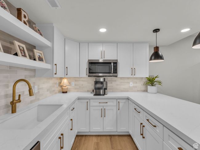 Kitchen featuring stainless steel microwave, open shelves, a sink, white cabinets, and decorative backsplash | Image 34
