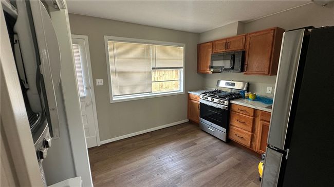 Kitchen with brown cabinets, light countertops, baseboards, appliances with stainless steel finishes, and wood finished floors | Image 5