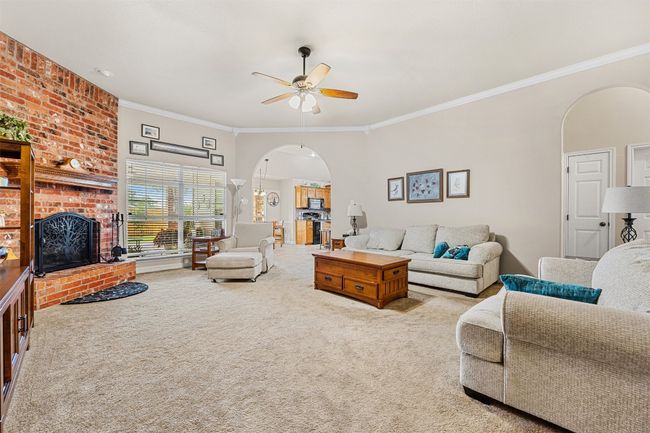 Living room with arched walkways, a brick fireplace, carpet floors, a ceiling fan, and ornamental molding | Image 6