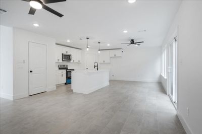 Kitchen featuring white cabinetry, an island with sink, ceiling fan, hanging light fixtures, and appliances with stainless steel finishes | Image 3