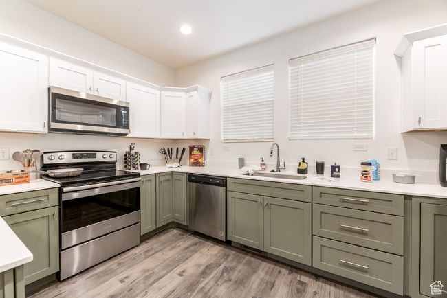 Kitchen with a sink, light countertops, light wood-type flooring, appliances with stainless steel finishes, and green cabinets | Image 8