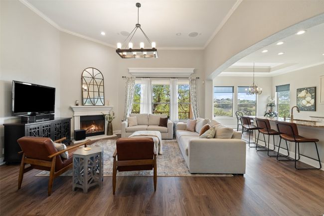 Living room featuring a lit fireplace, a chandelier, dark wood-style floors, and ornamental molding | Image 4