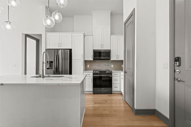 Kitchen featuring stainless steel appliances, a sink, decorative backsplash, light wood-style flooring, and white cabinets | Image 8