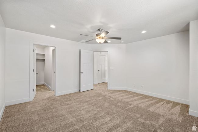 Primary Bedroom featuring light carpet, baseboards, private bathroom recessed lighting, a walk in closet, and a ceiling fan | Image 22