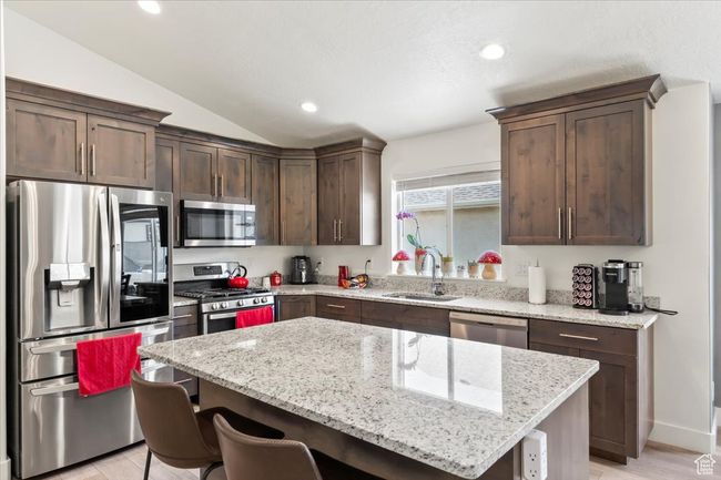 Kitchen featuring appliances with stainless steel finishes, a sink, dark brown cabinets, a center island, and a breakfast bar area | Image 7