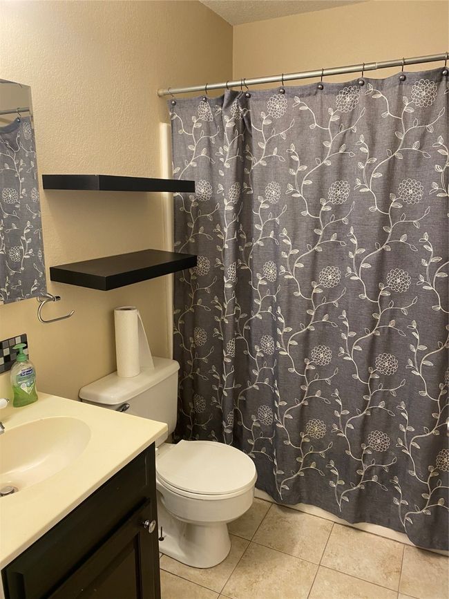 Full bath with curtained shower, vanity, tile patterned flooring, and toilet | Image 14