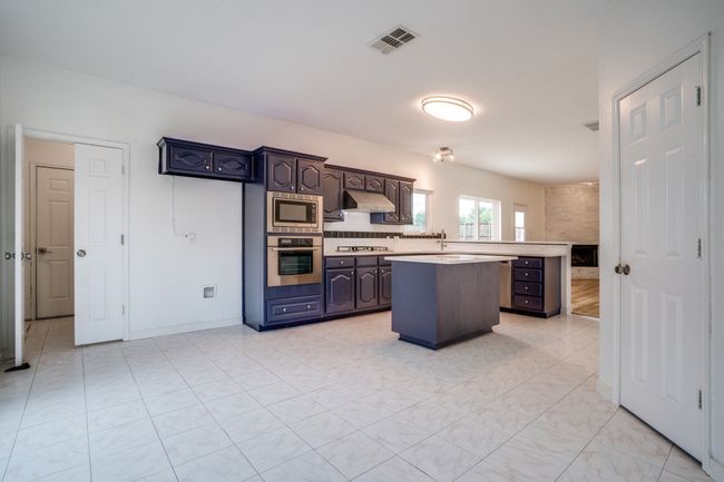 Kitchen featuring stainless steel appliances, under cabinet range hood, light countertops, a kitchen island, and dark brown cabinetry | Image 10