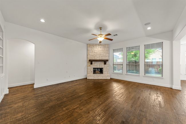Unfurnished living room featuring visible vents, a fireplace, baseboards, ceiling fan, and arched walkways | Image 14