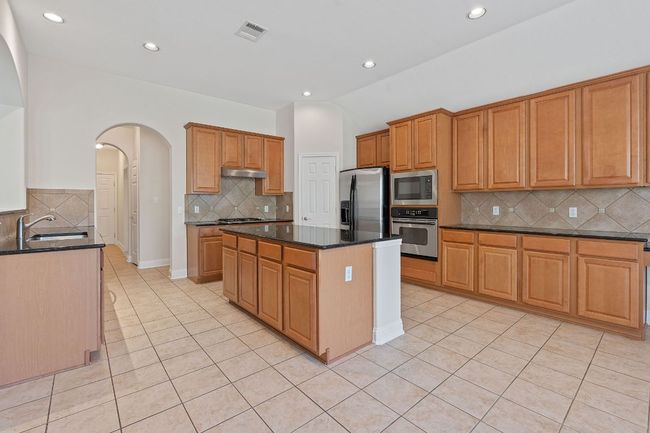 Kitchen with light tile patterned flooring, visible vents, stainless steel appliances, arched walkways, and under cabinet range hood | Image 11
