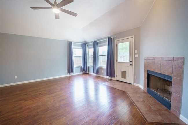 Living room featuring wood finished floors, a tile fireplace, a ceiling fan, baseboards, and vaulted ceiling | Image 10
