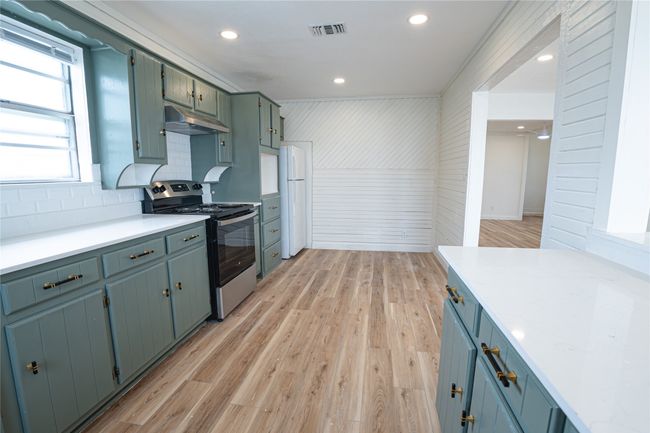 Kitchen with light wood finished floors, visible vents, under cabinet range hood, stainless steel electric range oven, and freestanding refrigerator | Image 12