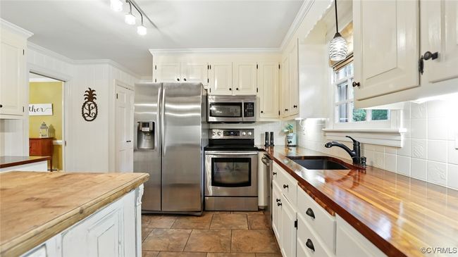 Kitchen with wood counters, appliances with stainless steel finishes, decorative backsplash, white cabinetry, and crown molding | Image 39