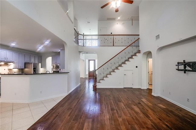 Unfurnished living room featuring arched walkways, a ceiling fan, a high ceiling, stairway, and hardwood / wood-style flooring | Image 9