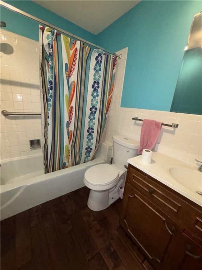Bathroom 1 featuring vanity, toilet, wood finished floors, tile walls, and shower / bath combo with shower curtain | Image 16