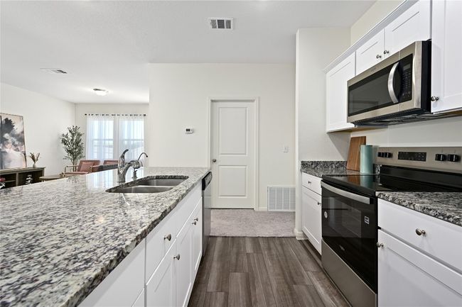 Kitchen featuring dark wood-style floors, stainless steel appliances, visible vents, a sink, and light stone countertops | Image 20