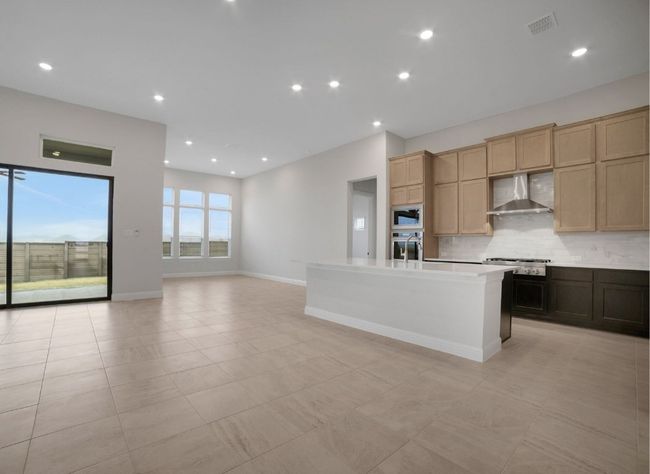 Kitchen featuring wall chimney range hood, light countertops, backsplash, a center island with sink, and appliances with stainless steel finishes | Image 8