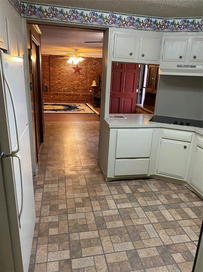 Kitchen with refrigerator, ventilation hood, stovetop, white cabinets, and a textured ceiling | Image 12