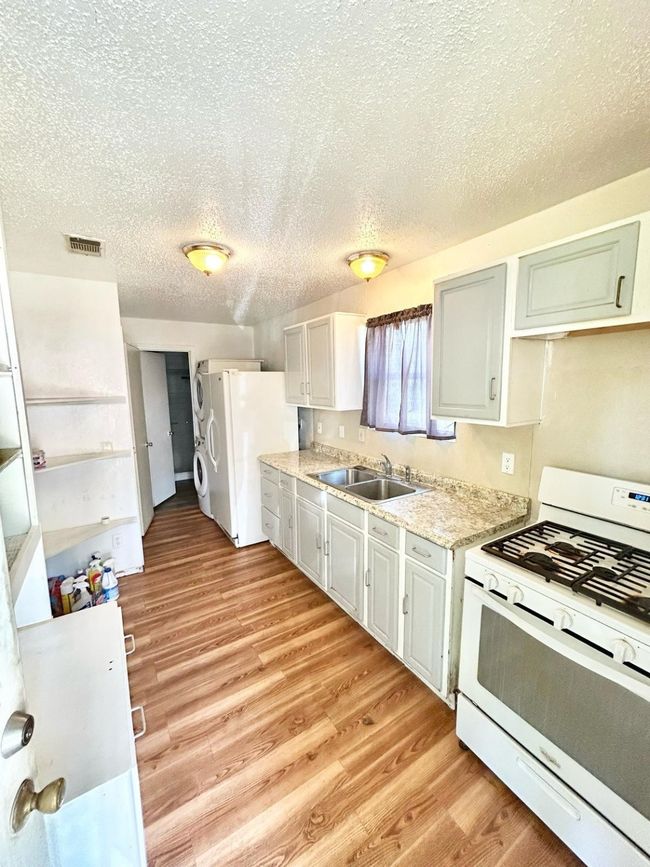 Kitchen with white appliances, a sink, a textured ceiling, and light wood-style floors | Image 5